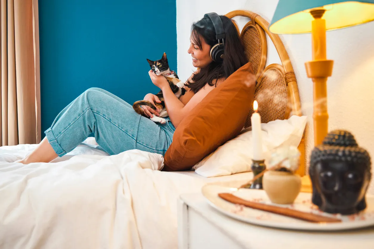 Woman sits on bed with cat burning candle