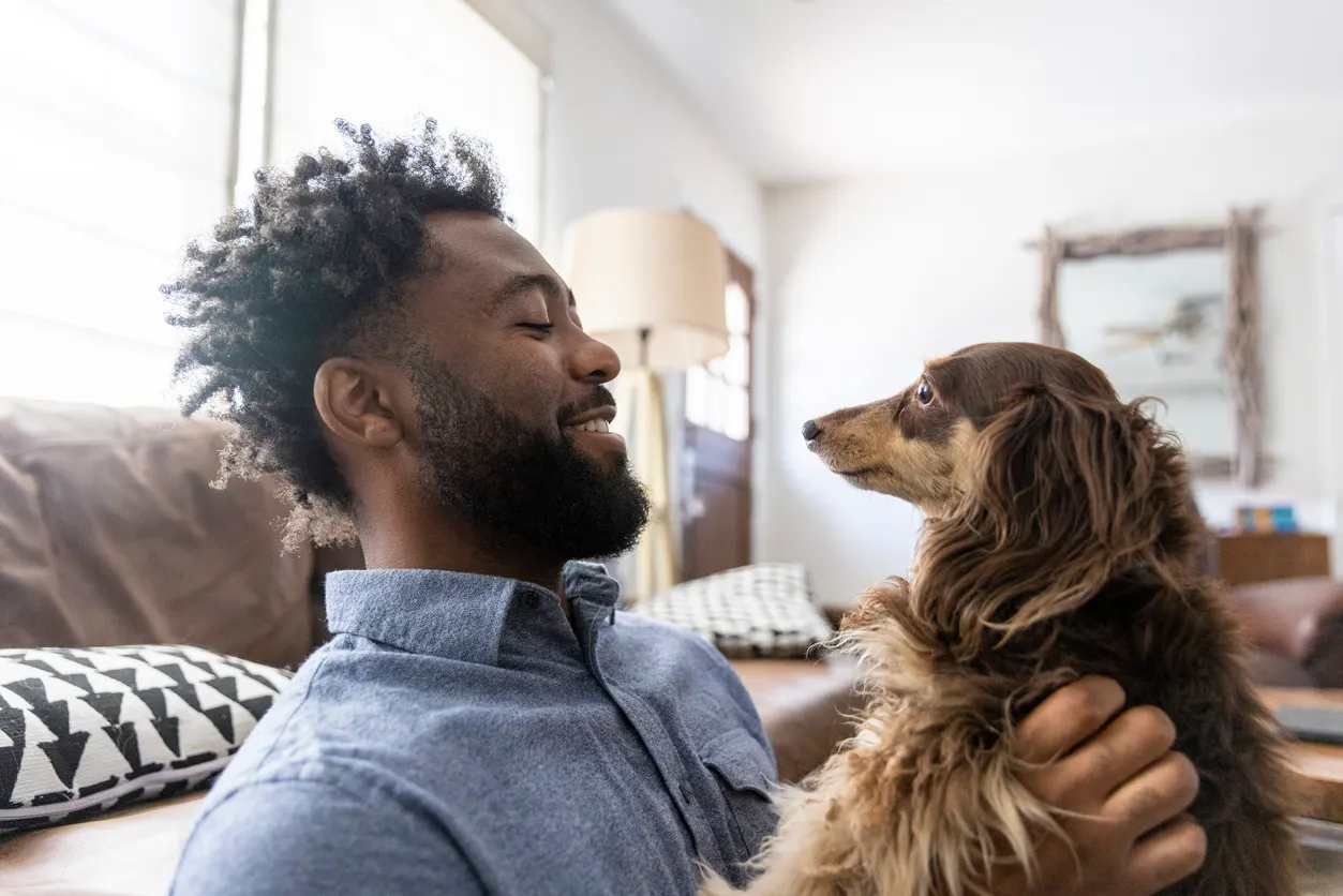 young man laughs and holds small dog in living room