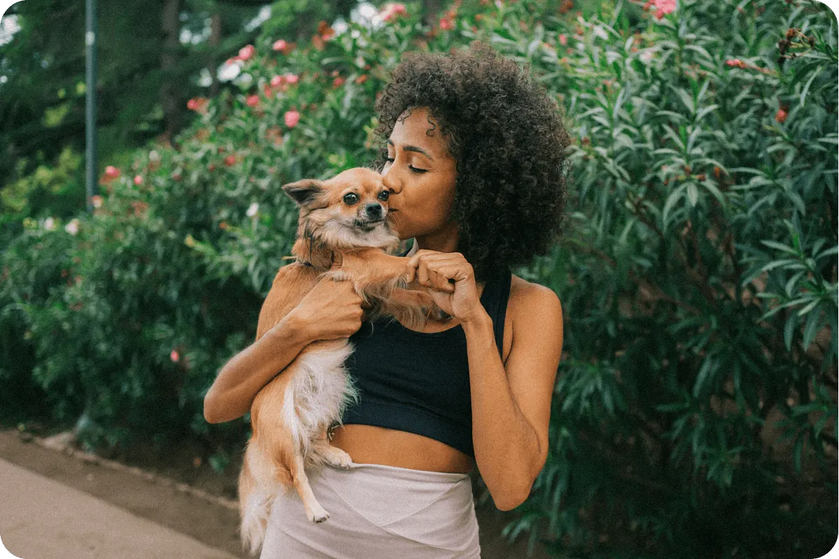 woman holds small affectionately dog outside