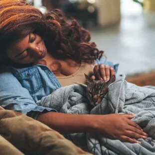 A woman holding a cat in a blanket while petting their head
