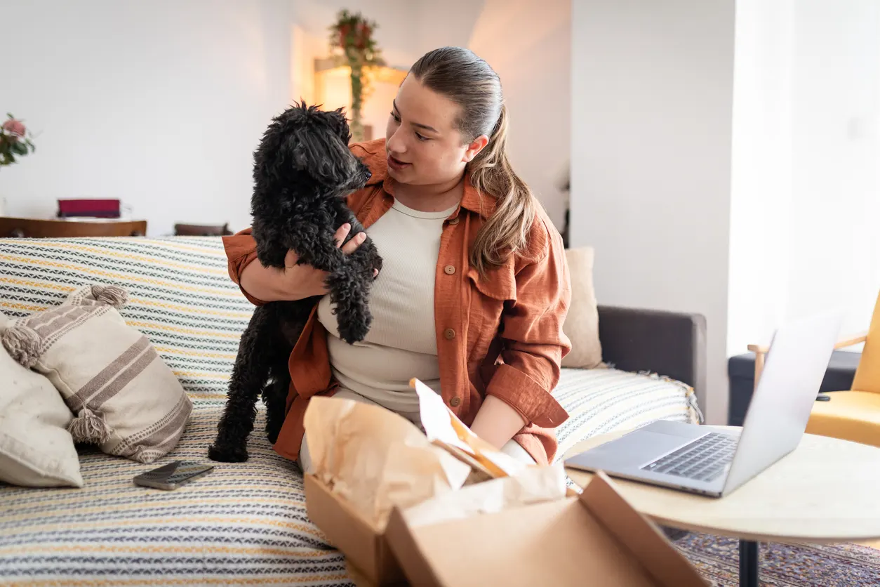 woman holds small dog while she opens package