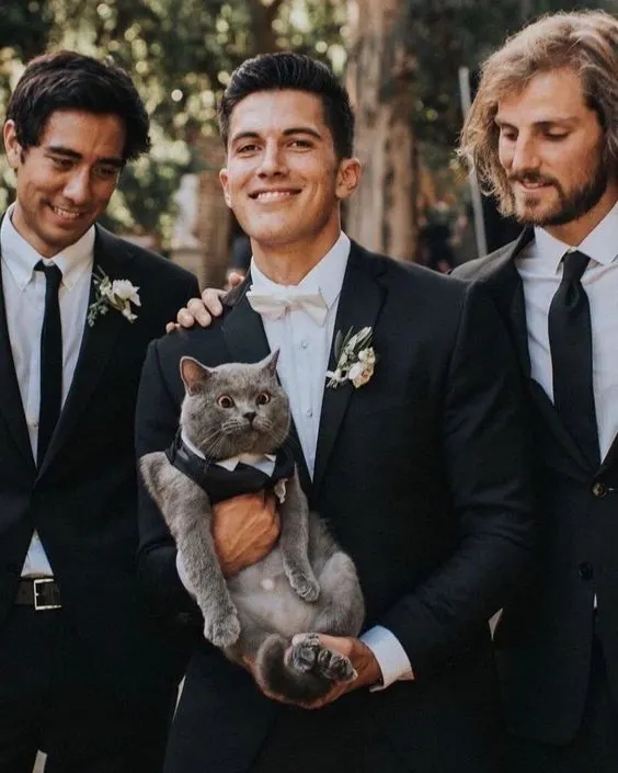 man posing with groomsman and holding cat