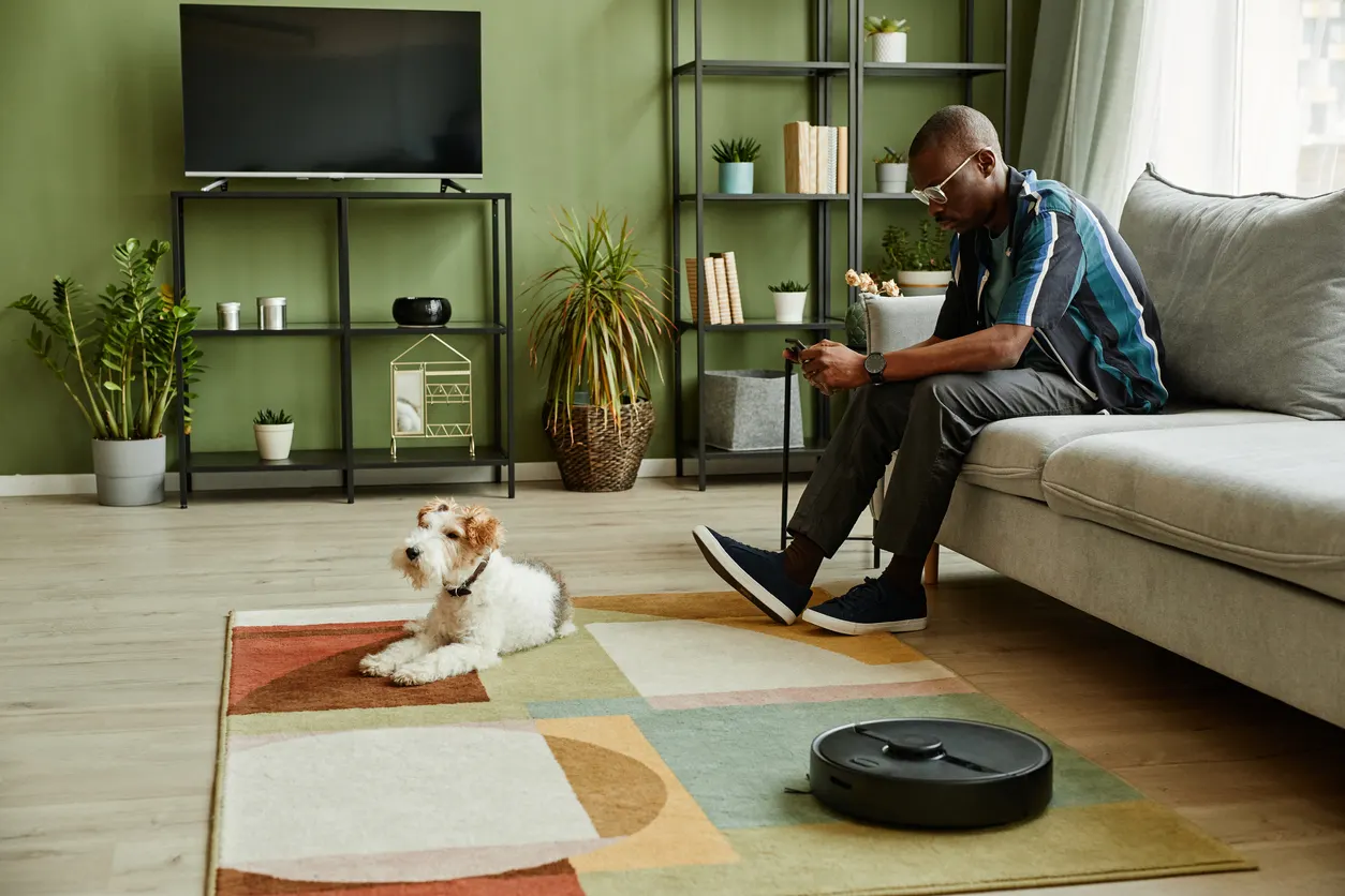 Man sitting with dog and robotic vacuum in living room