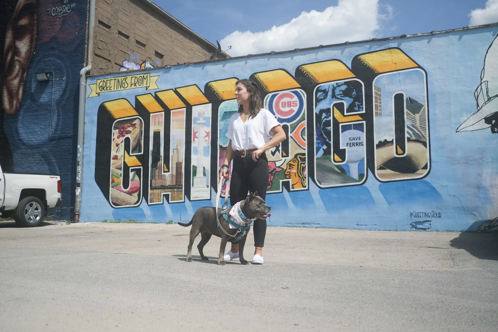 Woman stands with her dog in front of a mural
