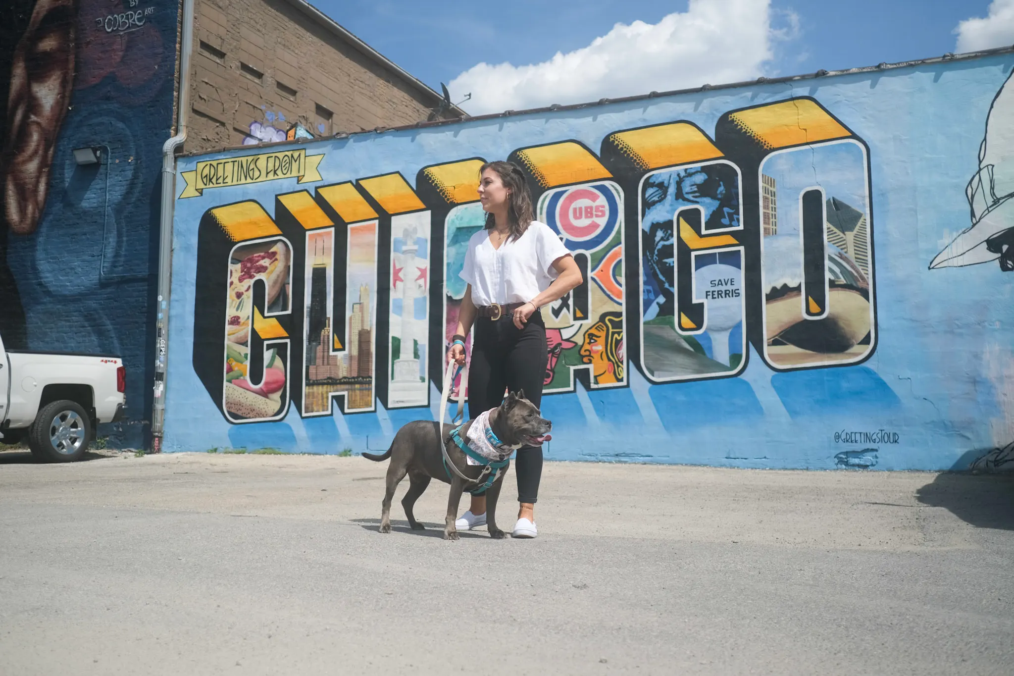 Woman stands with her dog in front of a mural