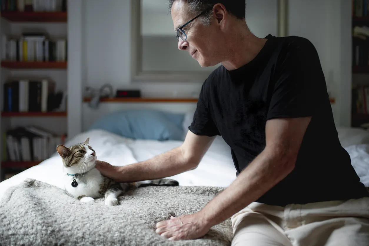 older man pets cat laying on bed