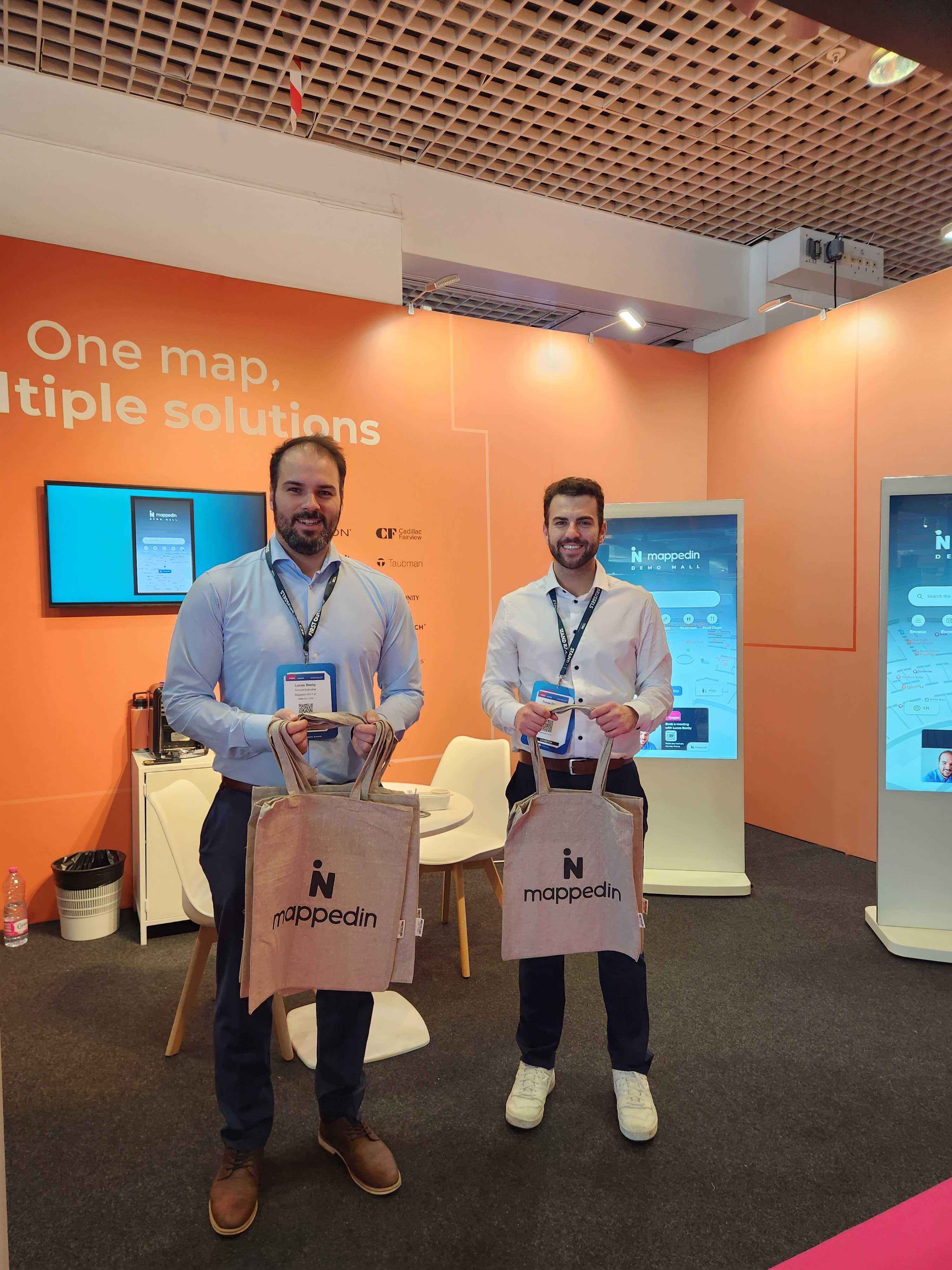 Two Mappedin employee's offering branded tote bags to MAPIC attendees