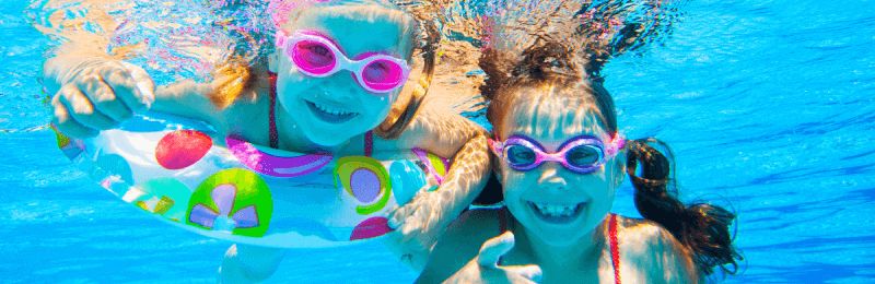 Two happy girls in goggles swimming under water.