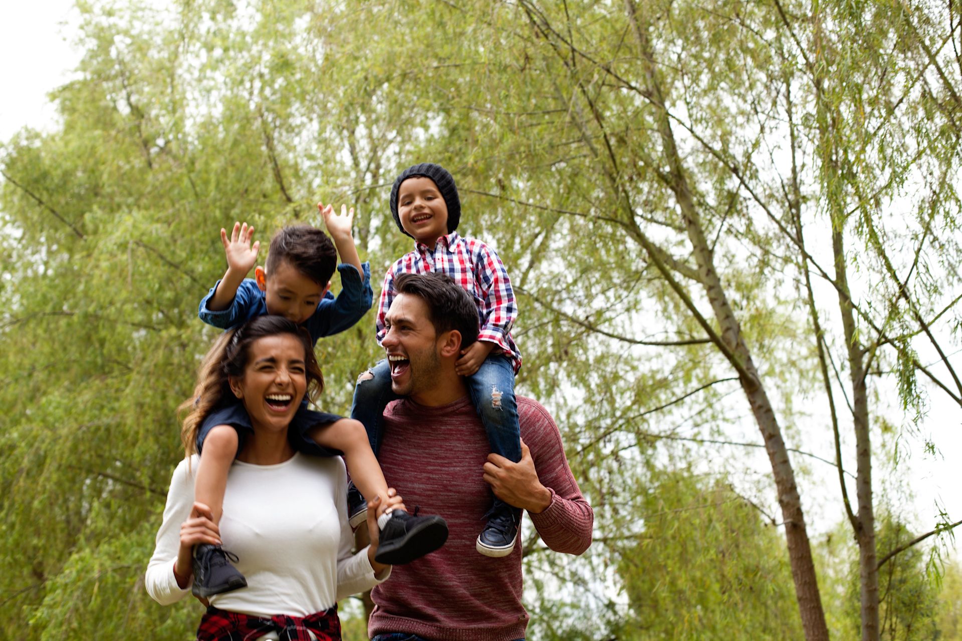 Young parents carrying their children on their shoulders and having fun outdoors