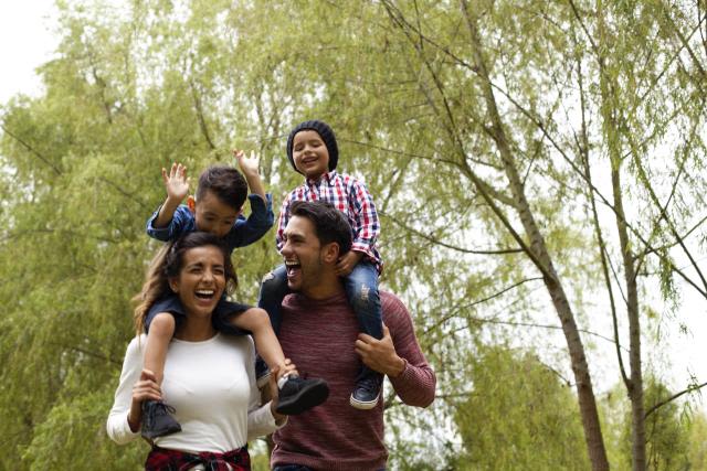 Young parents carrying their children on their shoulders and having fun outdoors