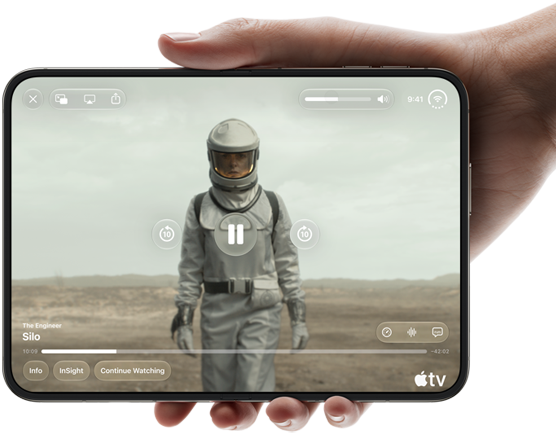 iPhone Duo, lo sostiene una mano, abierto en posición horizontal, completamente desplegado, la pantalla interior muestra la serie "Silo" de Apple TV
