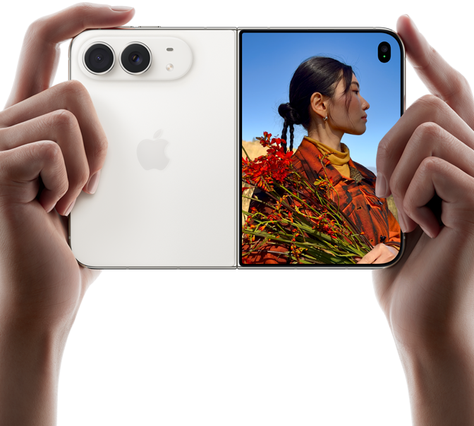 iPhone Duo, color blanco estrella, lo sostienen dos manos en posición horizontal, desplegado, el panel izquierdo muestra el sistema de dos cámaras Fusion traseras de 48 MP, el panel derecho muestra a una persona a quien le toman una foto en la pantalla exterior, la persona fotografiada puede verse en la pantalla con Duo Preview mientras le toman la foto