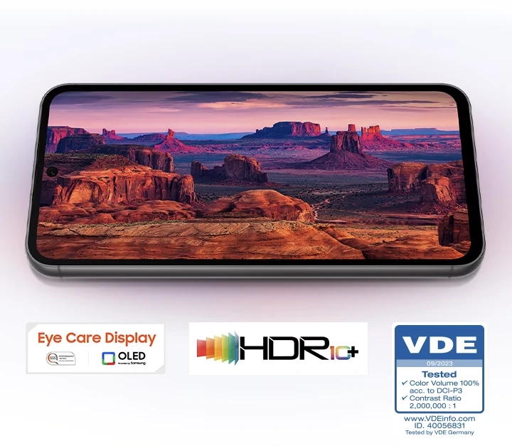 Un dispositivo Galaxy S23 FE muestra, en pantalla completa, un paisaje de montaña en rojo y púrpura capturado por la cámara. Se lee la marca Eye Care Display, rendimiento SGS comprobado, www.sgs.com/performance, OLED proporcionado por Samsung. Logotipo HDR10+. Logotipo de VDE con textos 09/2023, volumen de color probado 100 % según la relación de contraste DCI-P3 2 000 000:1. Id. de www.VDEinfo.com. 40056831 Probado por VDE Alemania.