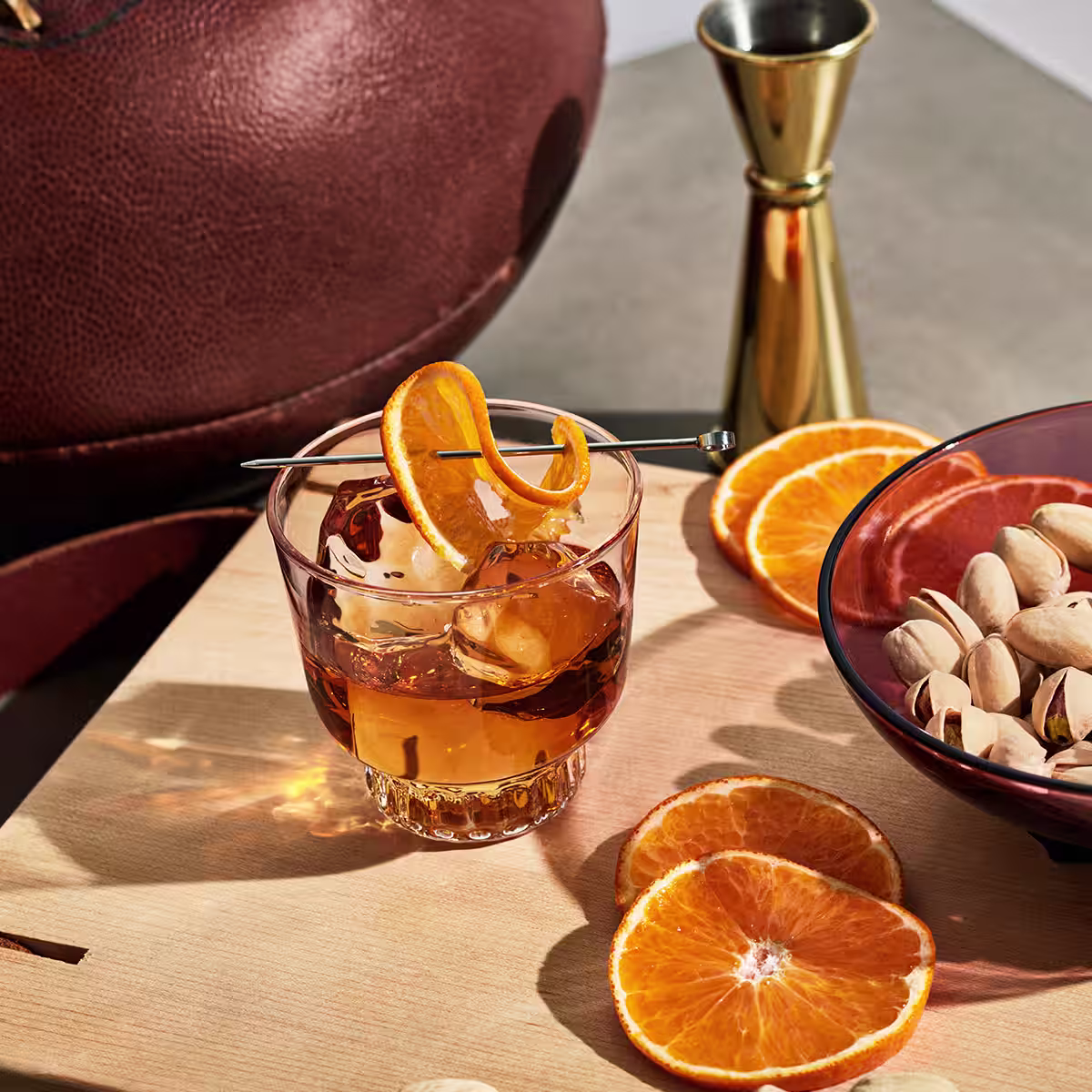 An Old Fashioned cocktail on a cutting board next to orange slices 