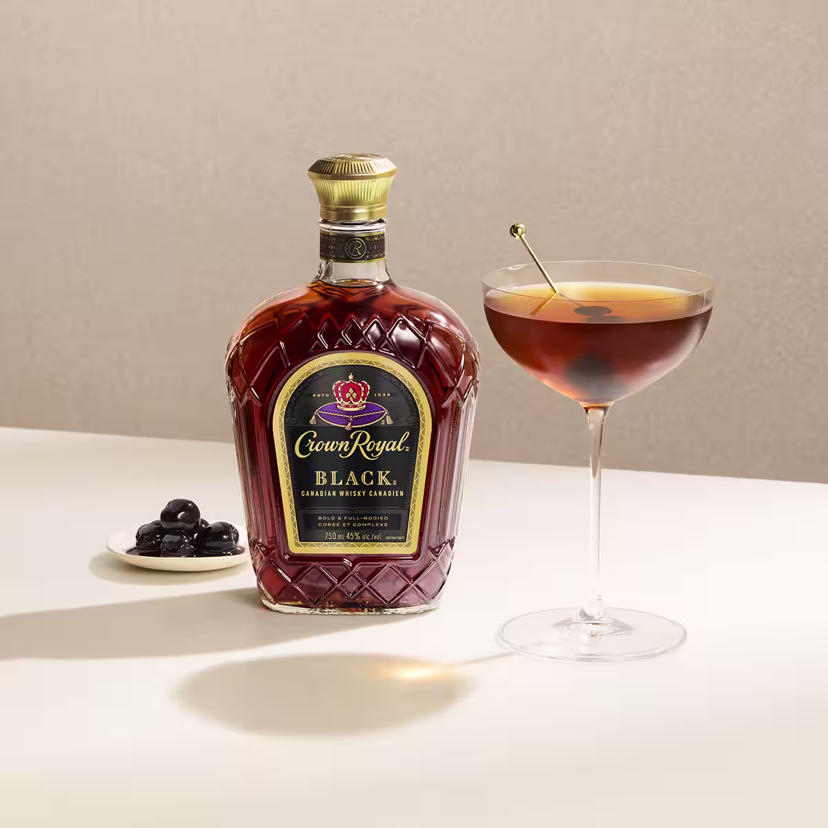 A bottle of Crown Royal Black next to a Black Manhattan cocktail on a table