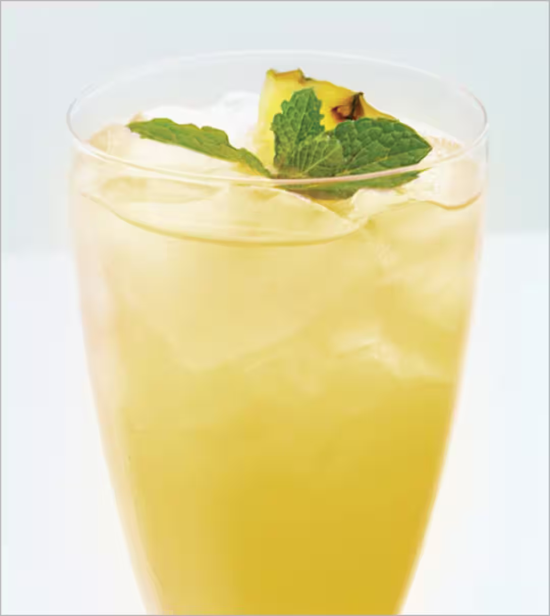 A yellow Apple Fizz cocktail garnished with a pineapple slice and a sprig of mint