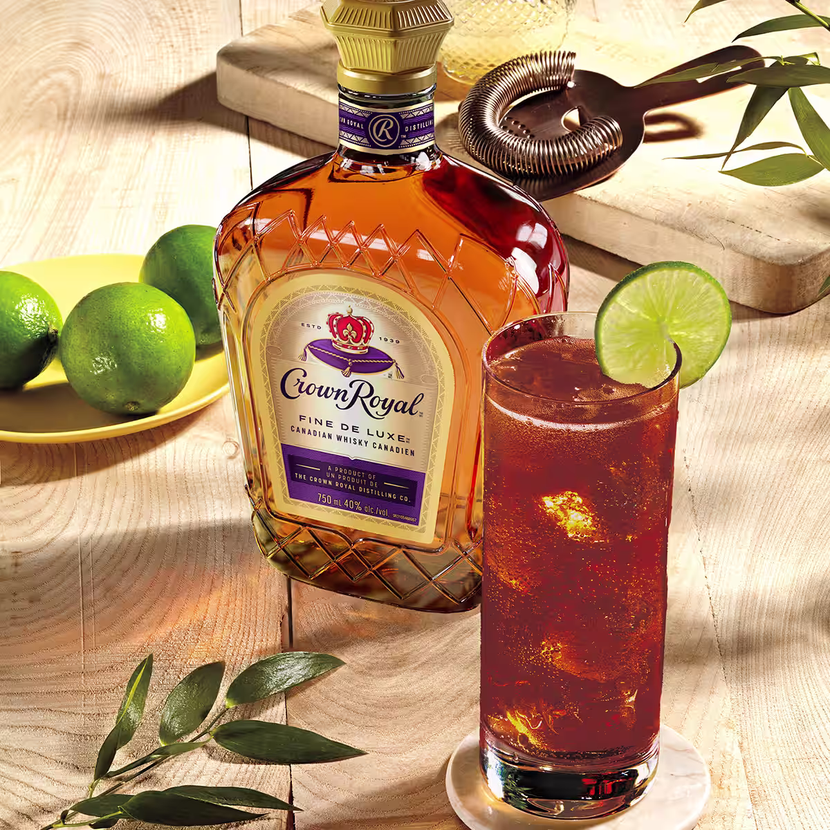 A bottle of Crown Royal De Luxe next to a Whisky & Cola cocktail