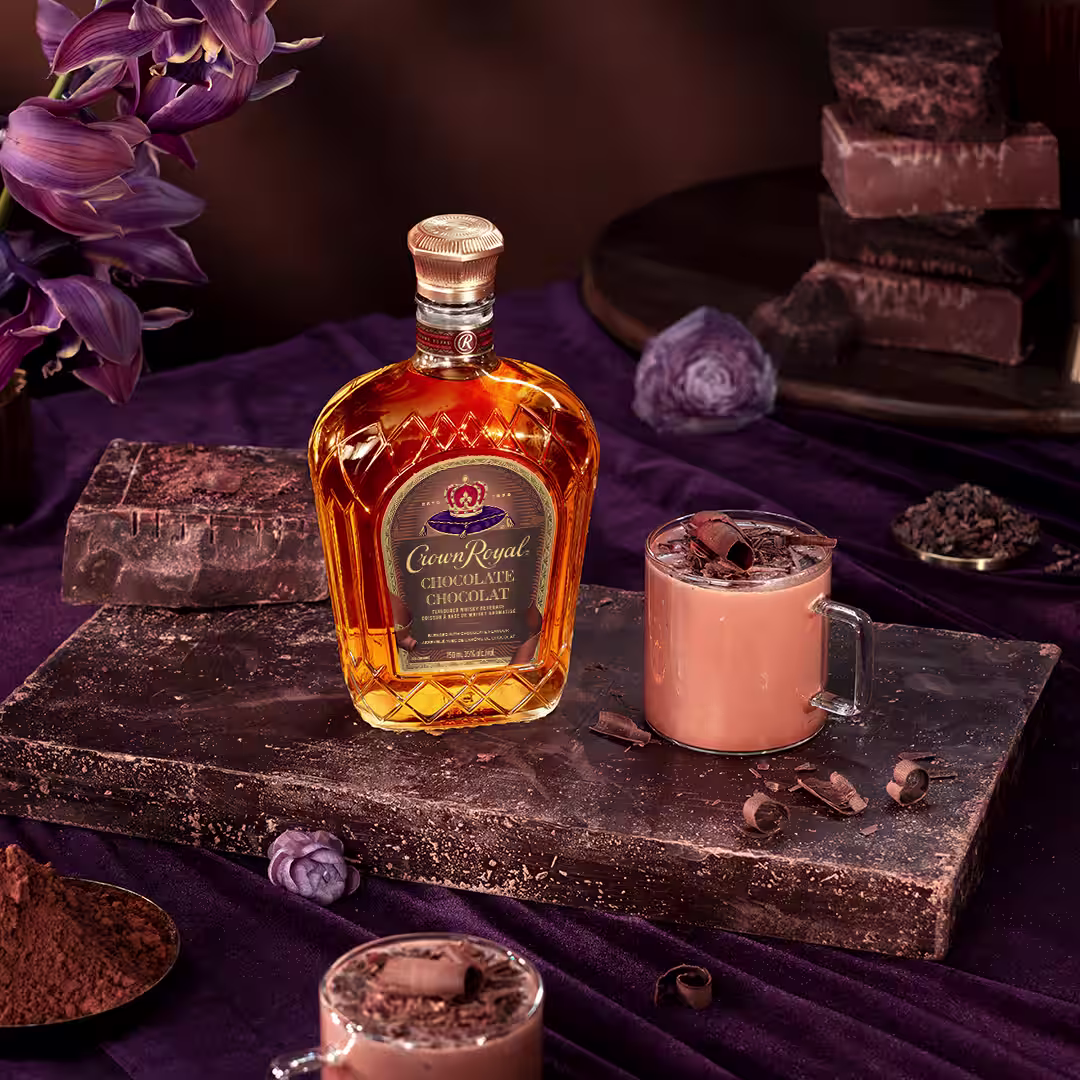 A bottle of Crown Royal Chocolate next to a whisky and hot chocolate cocktail garnished with chocolate shavings
