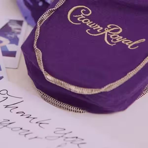 A Crown Royal purple bag on a table next to a thank you note