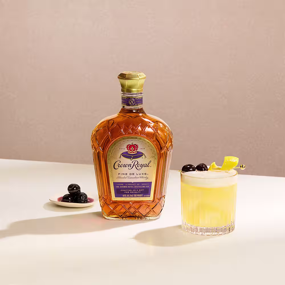 A bottle of Crown Royal De Luxe next to a whisky sour cocktail