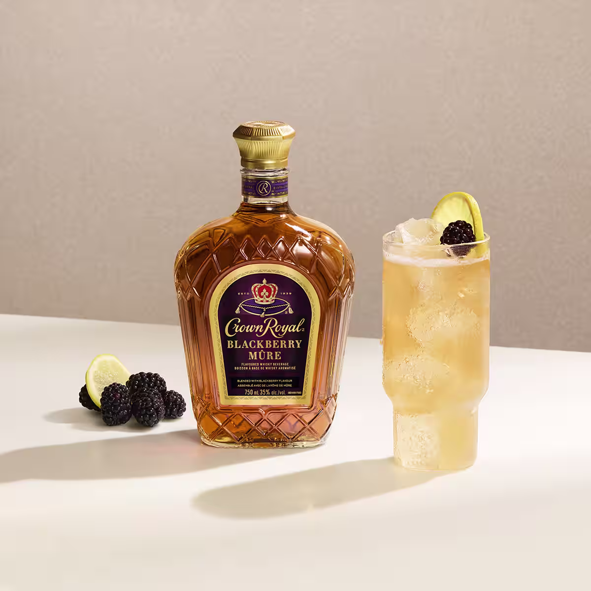A blackberry whisky lemonade cocktail on a table next to a bottle of Crown Royal Blackberry