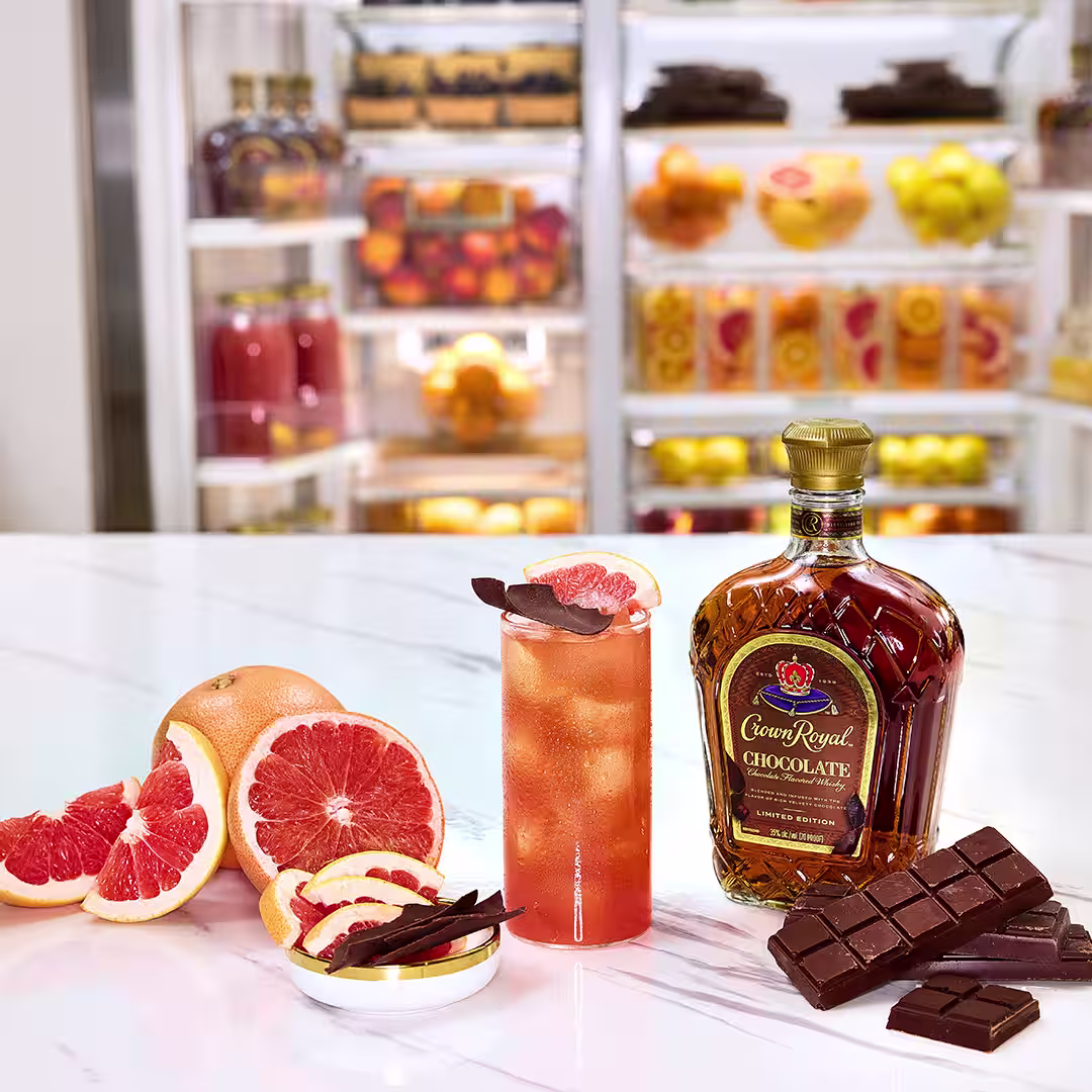 A bottle of Crown Royal Chocolate next to a chocolate paloma cocktail garnished with chocolate shavings and a grapefruit slice