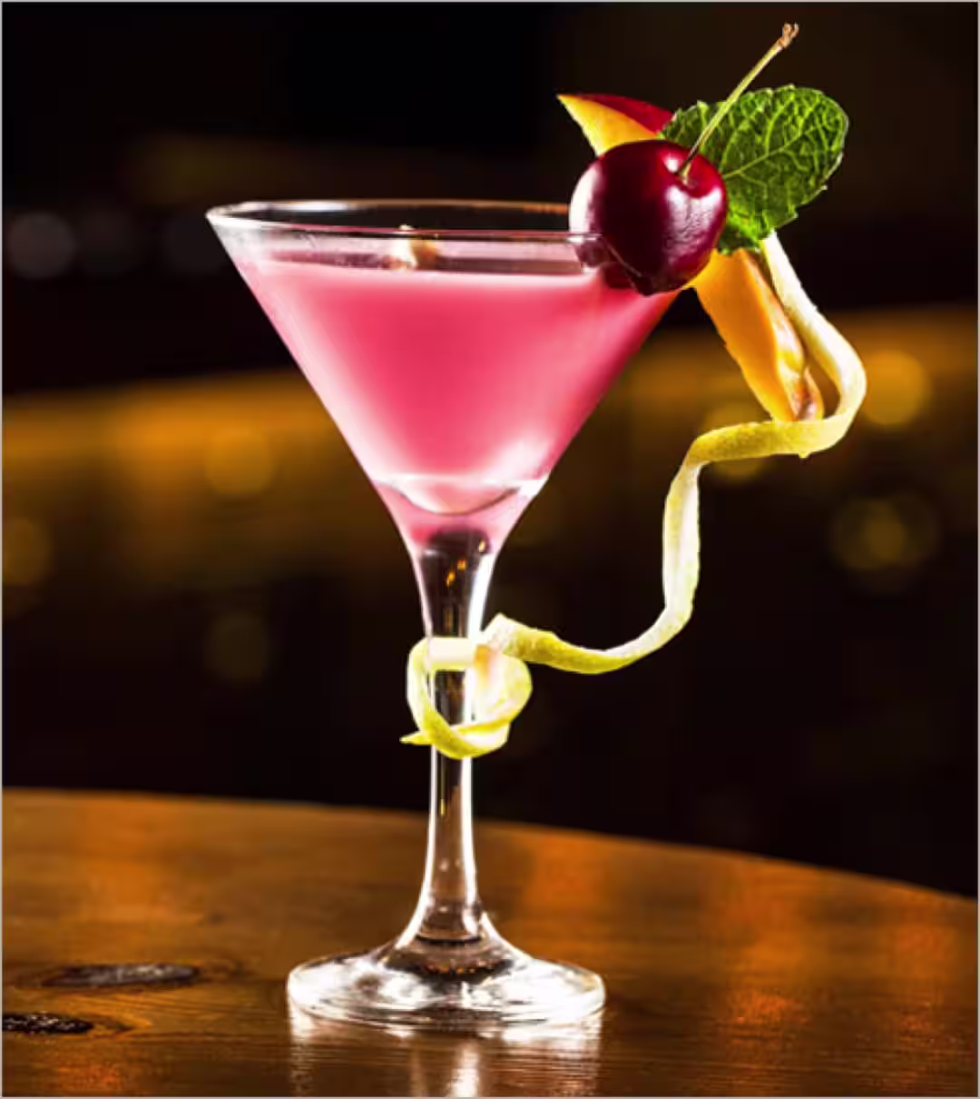 A Pink Royalty cocktail in a martini glass garnished with a cherry, mint leaf, and a apple slice
