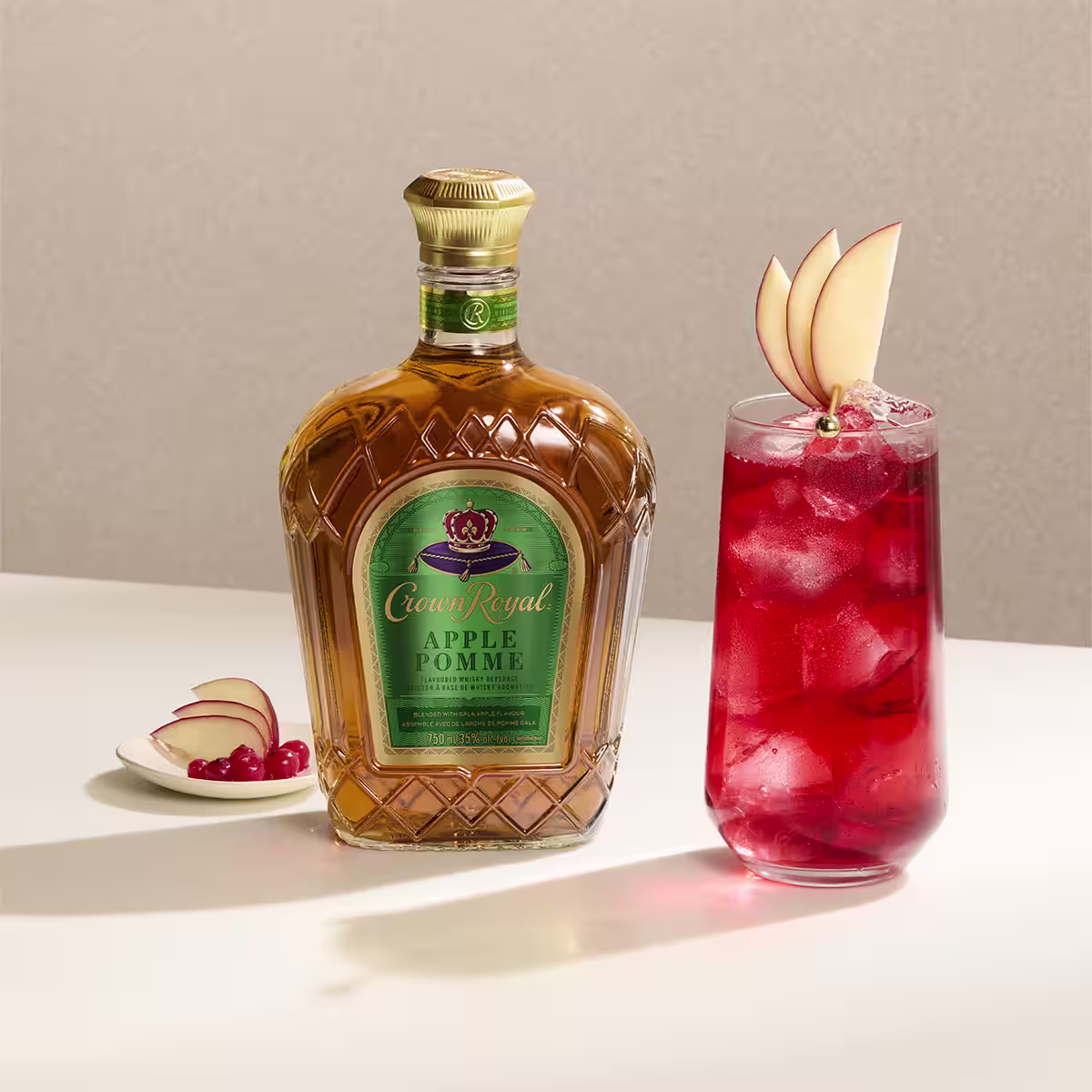 A apple cranberry cocktail next to a bottle of Crown Royal Apple