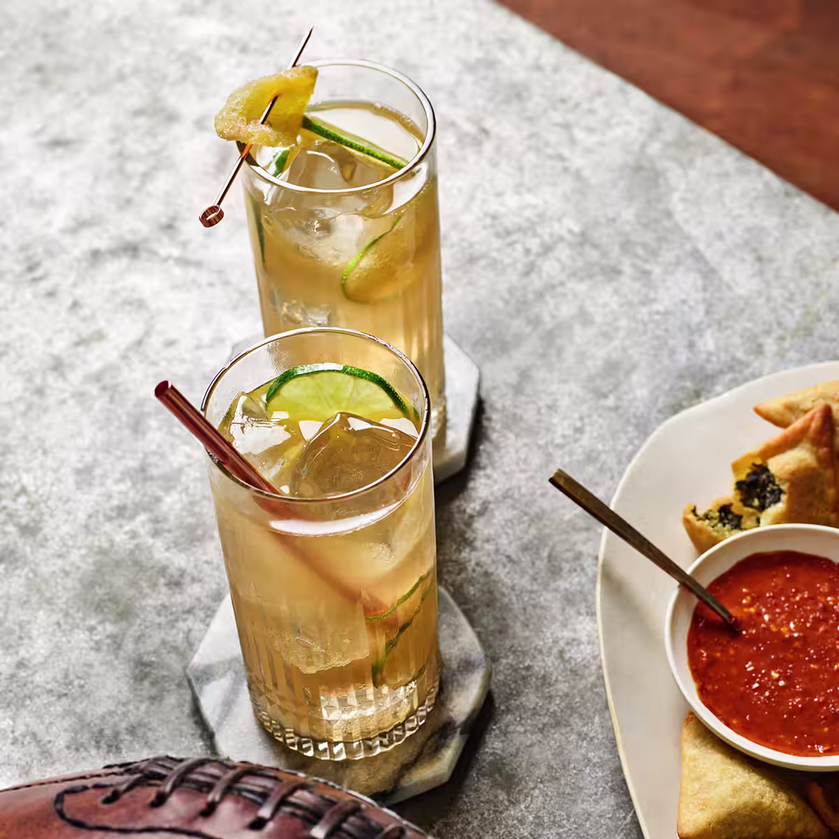 Two Black Whisky Ginger Ale cocktails garnished with lime peels on a table 