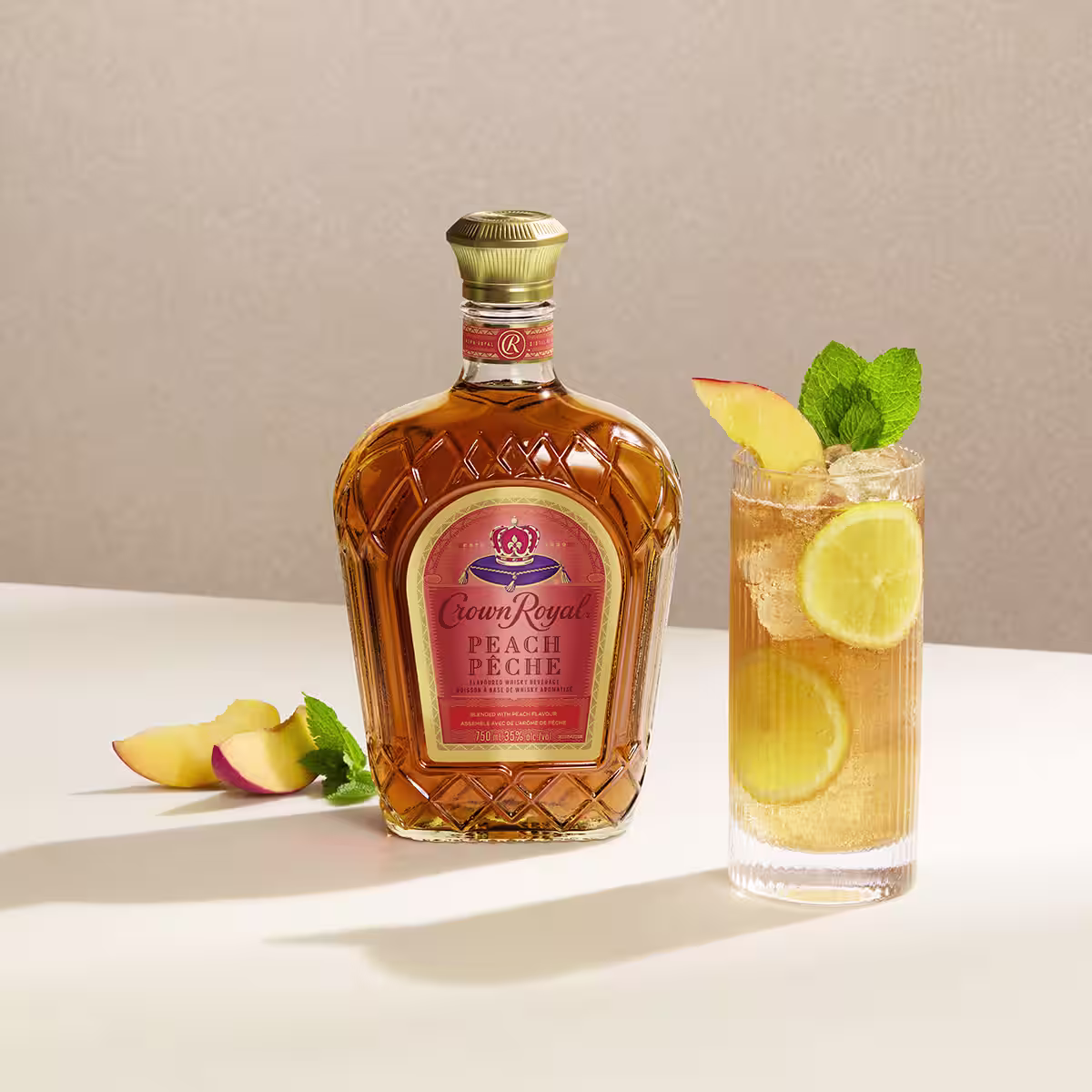 A peach tea cocktail on a table next to a bottle of Crown Royal Peach
