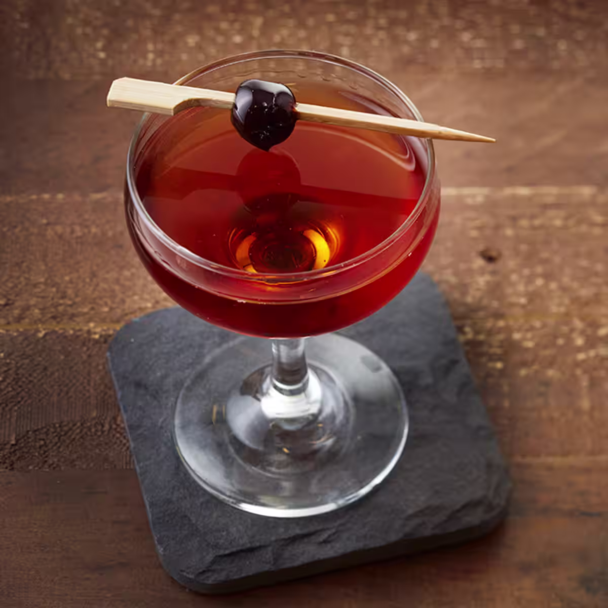 A King of Manhattan cocktail on a table, garnished with a maraschino cherry
