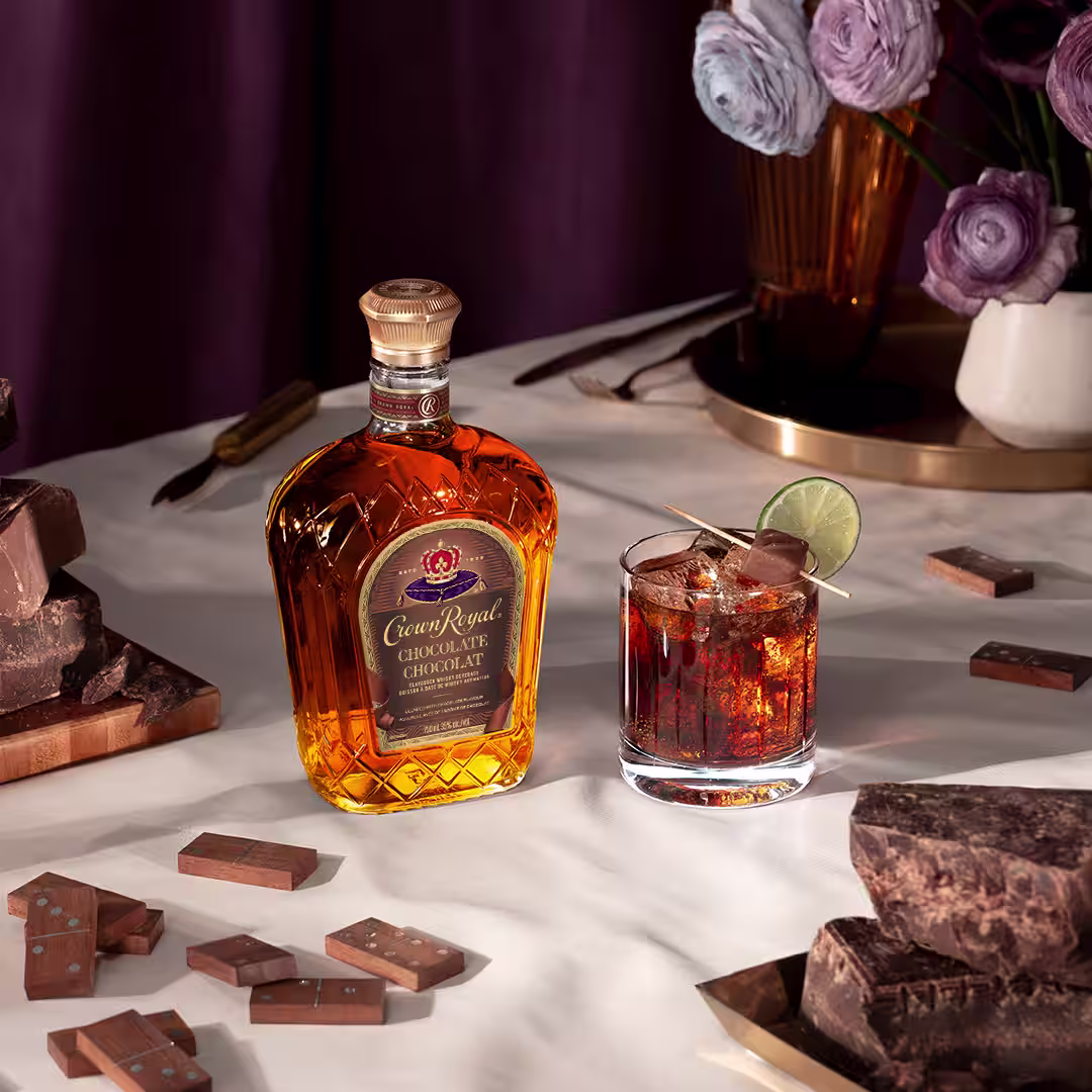 A bottle of Crown Royal Chocolate next to a whisky and cola drink garnished with a lime wheel