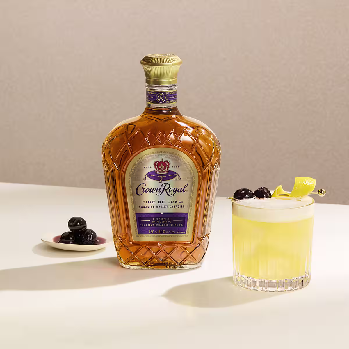 A whisky sour cocktail on a table next to a bottle of Crown Royal DeLuxe