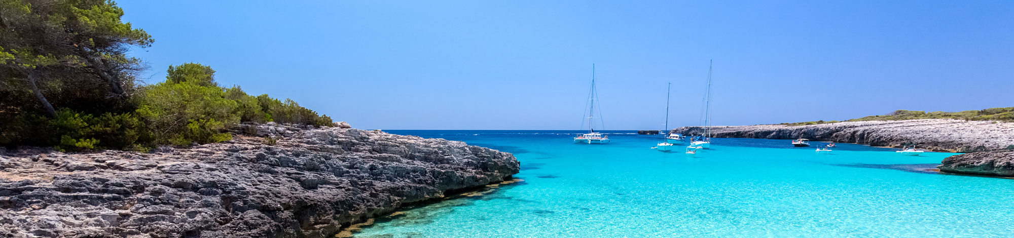 Türkisfarbene Bucht mit weißen Segelbooten auf der Balearen Insel Menorca 