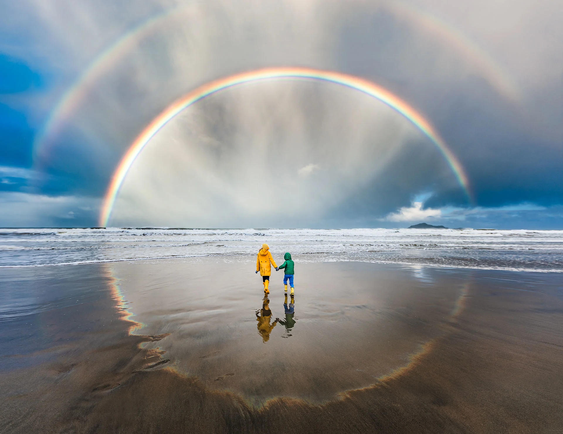 Rainbow reflecting on wet beach with children in the middle