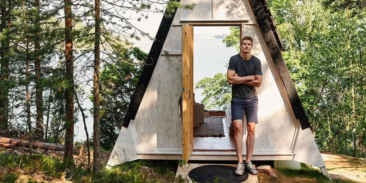 Image of Lauri Markkanen standing in front of Nolla Cabin, with forest and ocean in the background.