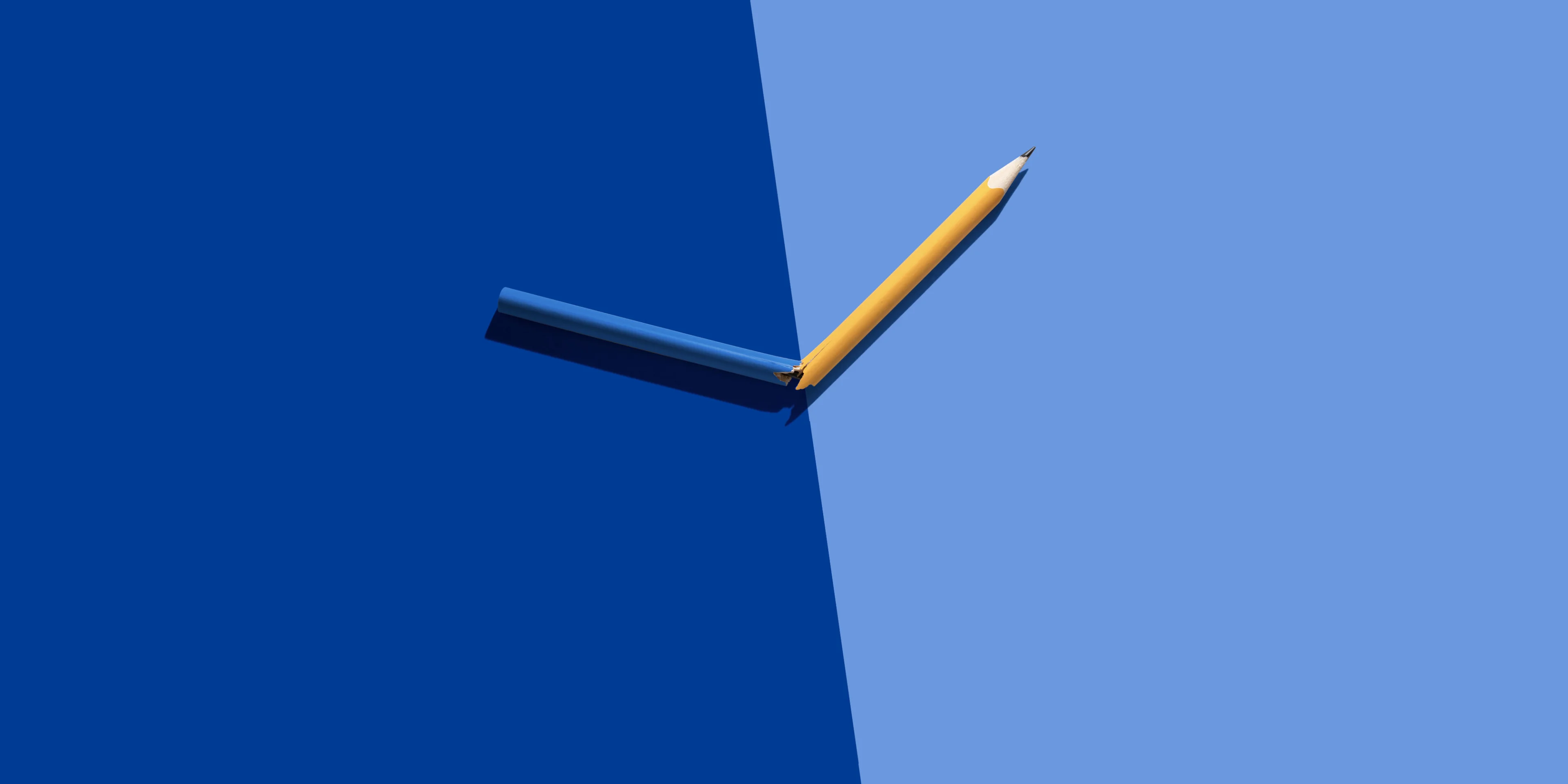 Pen snapped in half on a background of two halves of different shades of blue | Neste