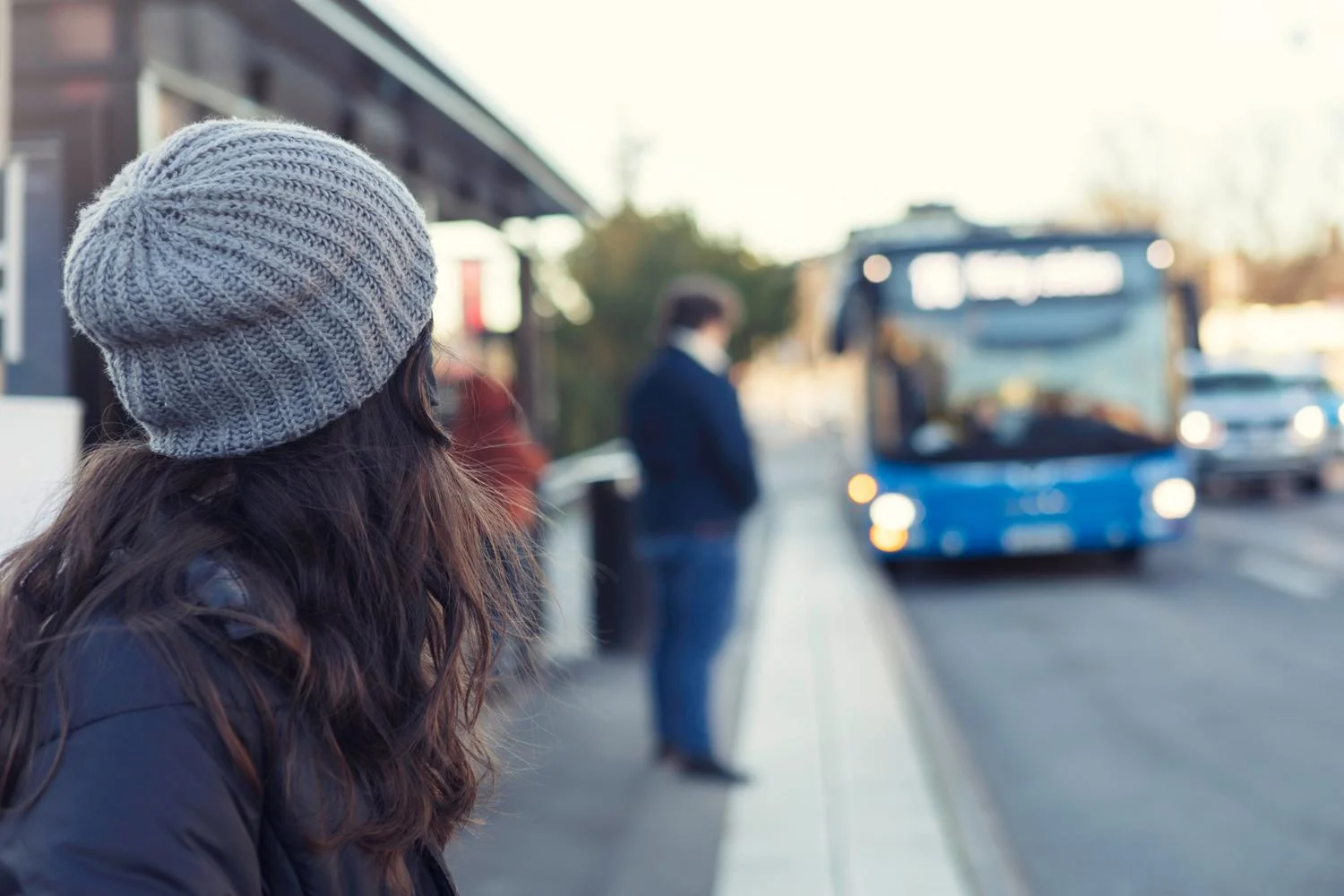 A bus arrives at a bus stop where people are waiting.
