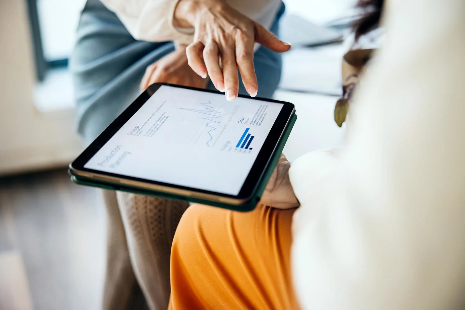 A close up of two business colleagues using a digital tablet to look over some sales data together at the office.