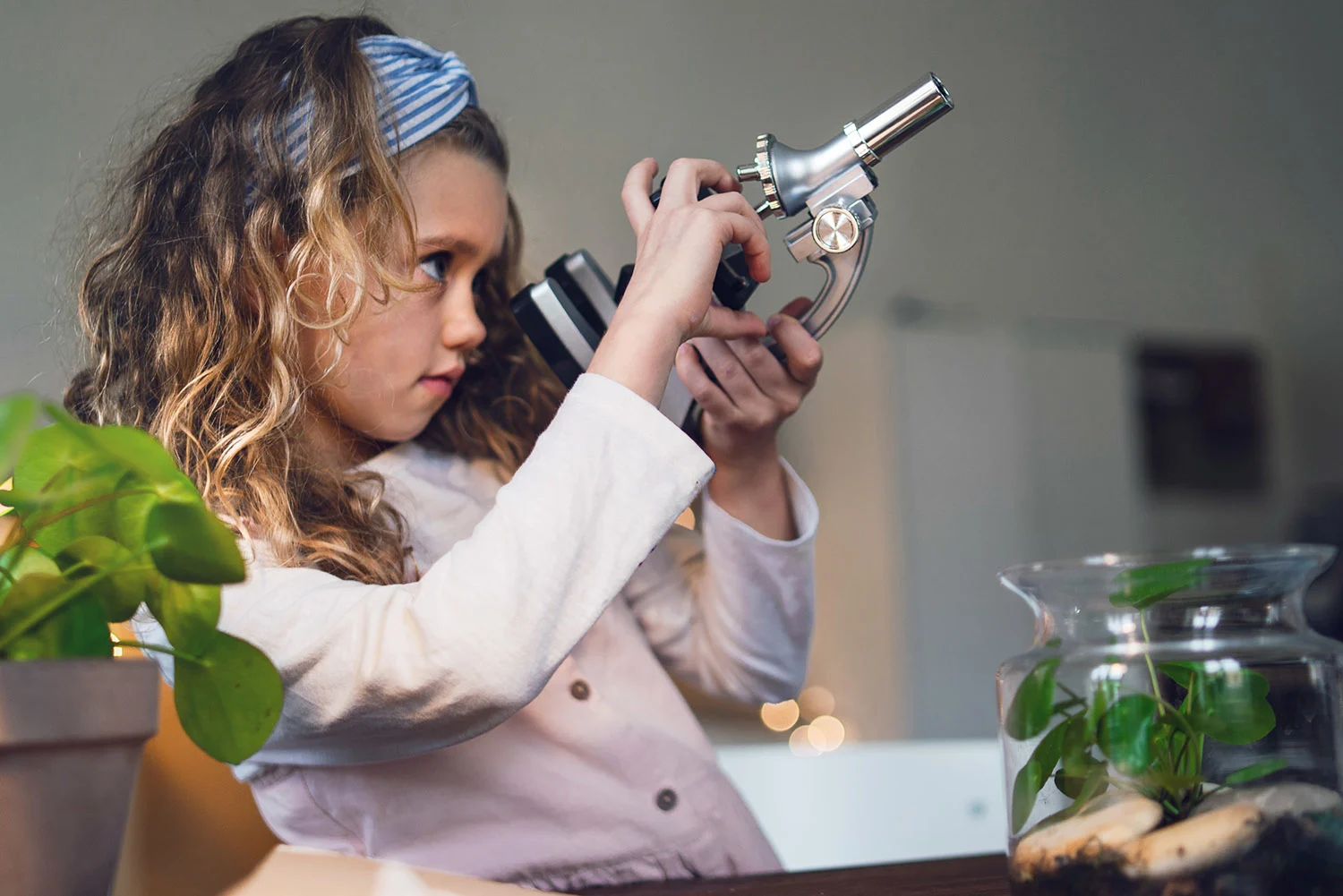 Girl looking at micro-telescope with plants on the table | Neste