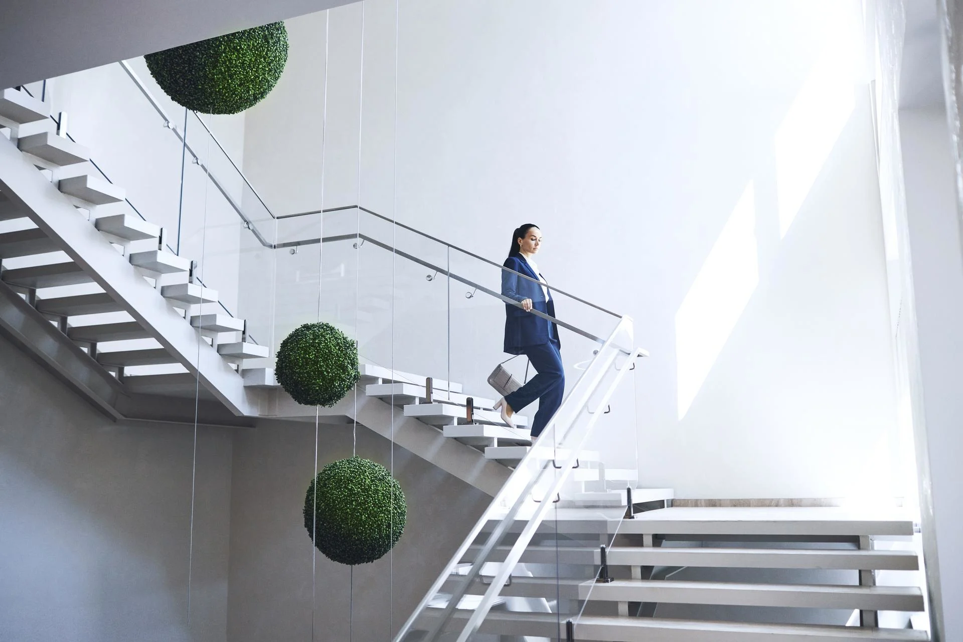 Wide angle shot of Caucasian woman in business suit carrying purse going downstairs holding on handrail in modern office building.