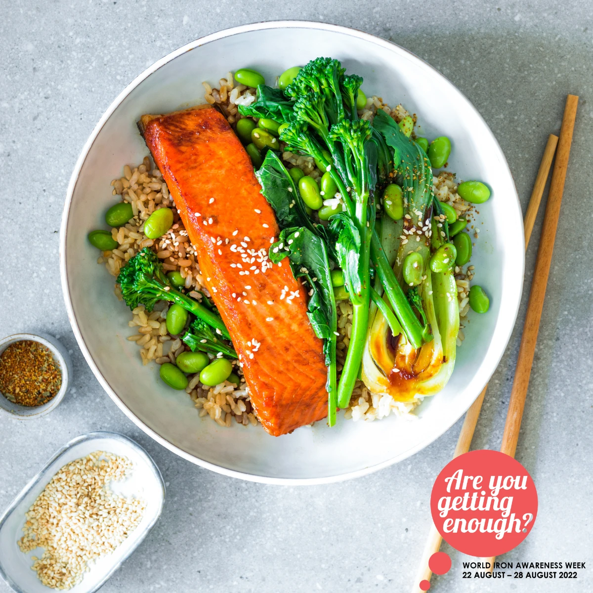 Teriyaki Salmon and Broccolini Rice Bowls with edamame beans on grey background with sesame seeds and soy sauce