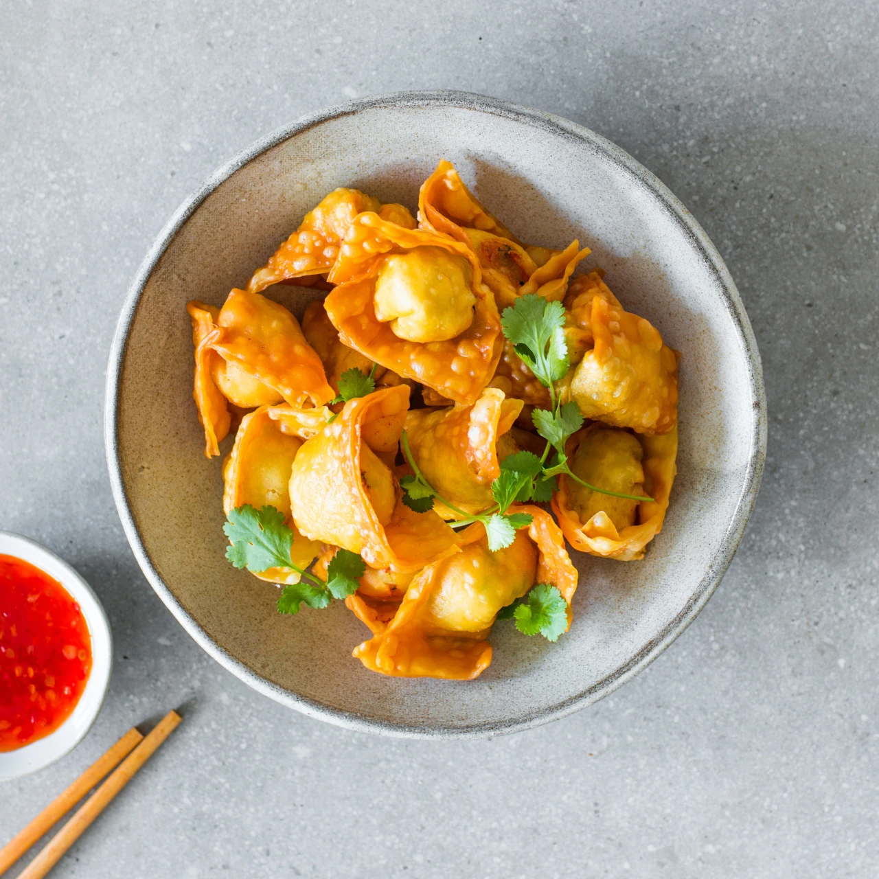 Cripsy golden Tarakihi, Coriander and Ginger Wontons on grey background with coriander leaves, wooden chopsticks and sweet chilli sauce