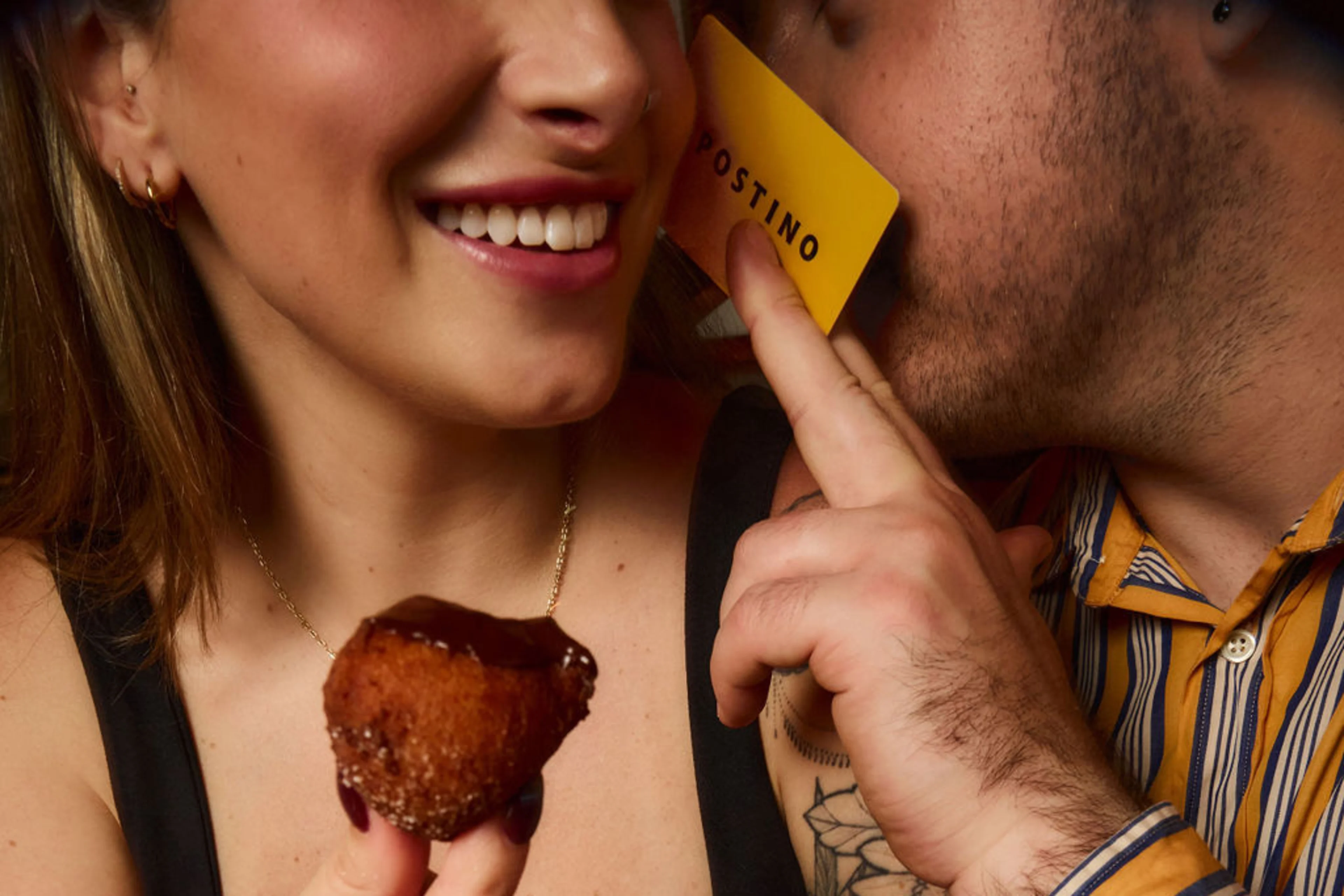 Man hiding his lips with a Postino gift card while whispering in a woman's ear.