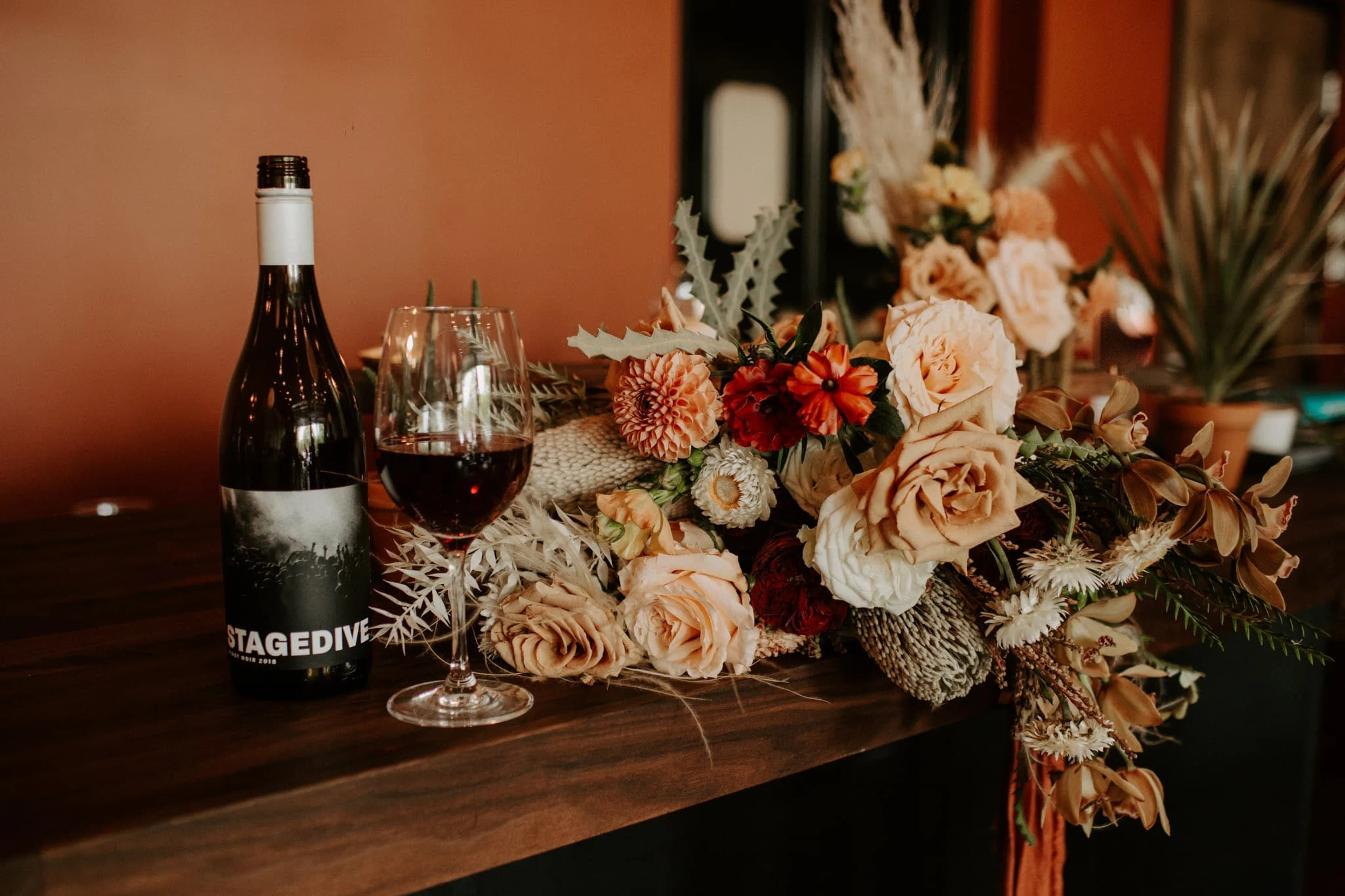 A wooden table with flowers and a glass and bottle of wine