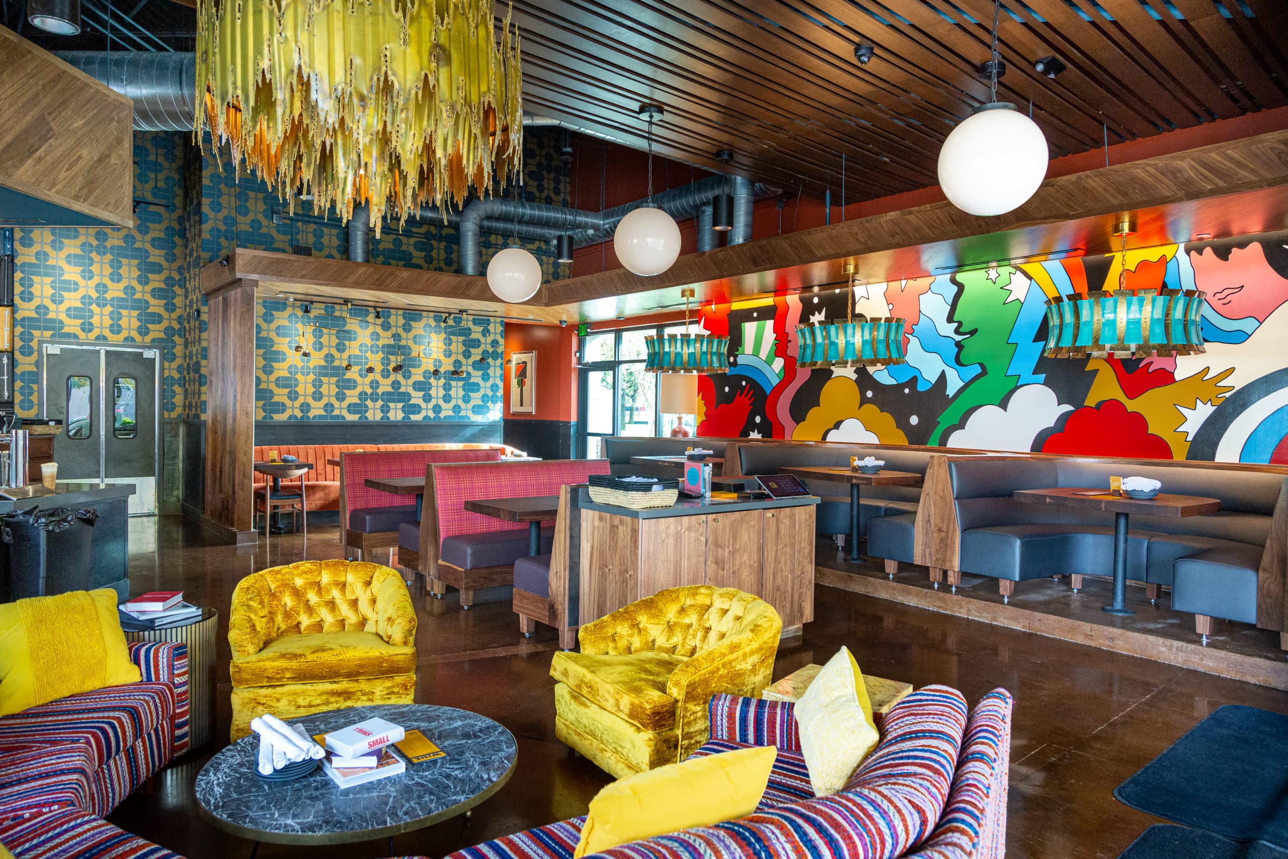 A large restaurant with yellow chairs, colorfully painted walls, and yellow glass chandeliers. 