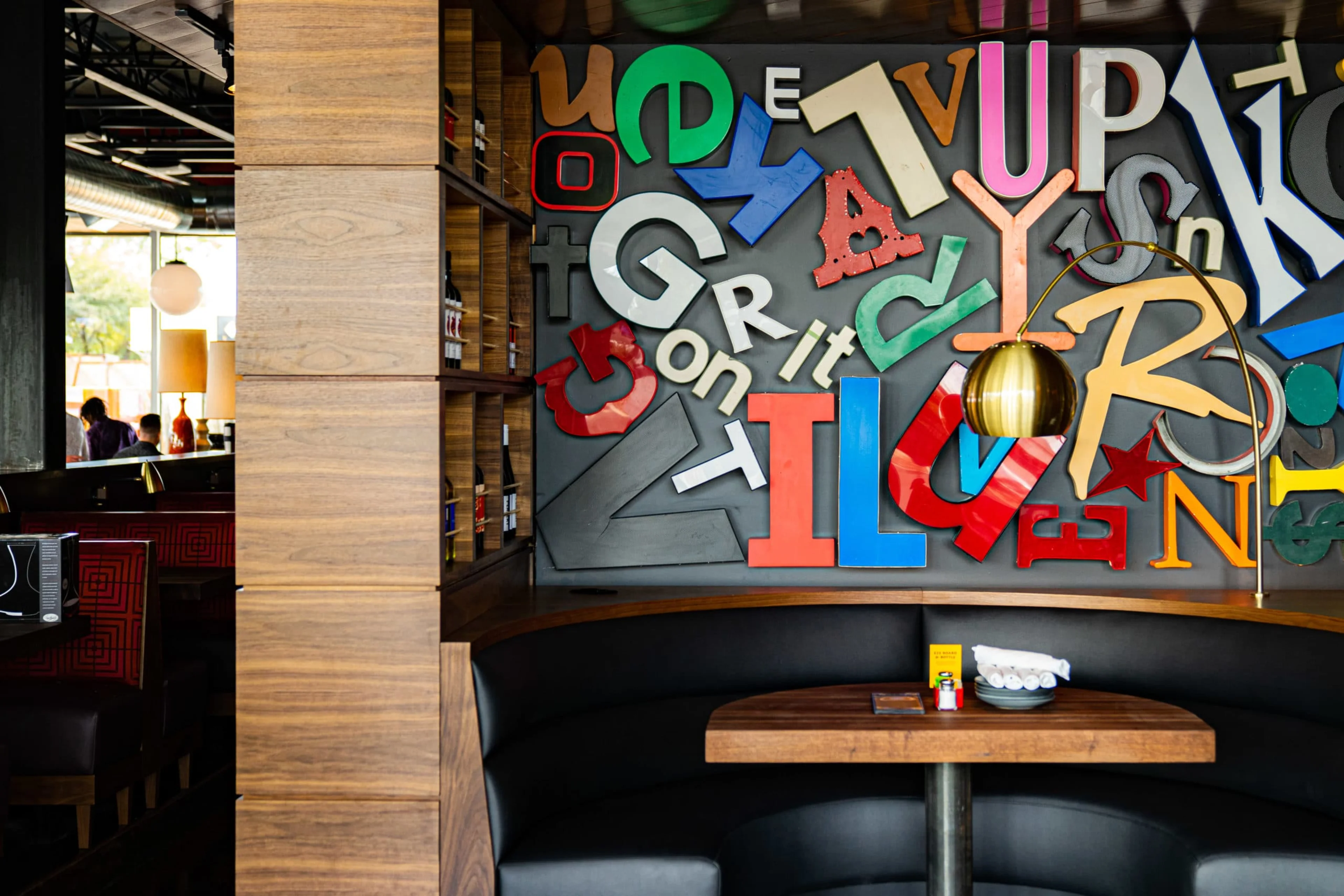 A booth table with large colorful letters on the wall behind it.