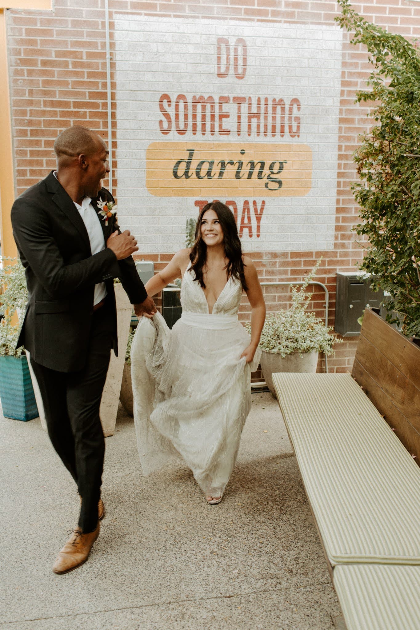 A bride and groom smile while walking and holding hands.