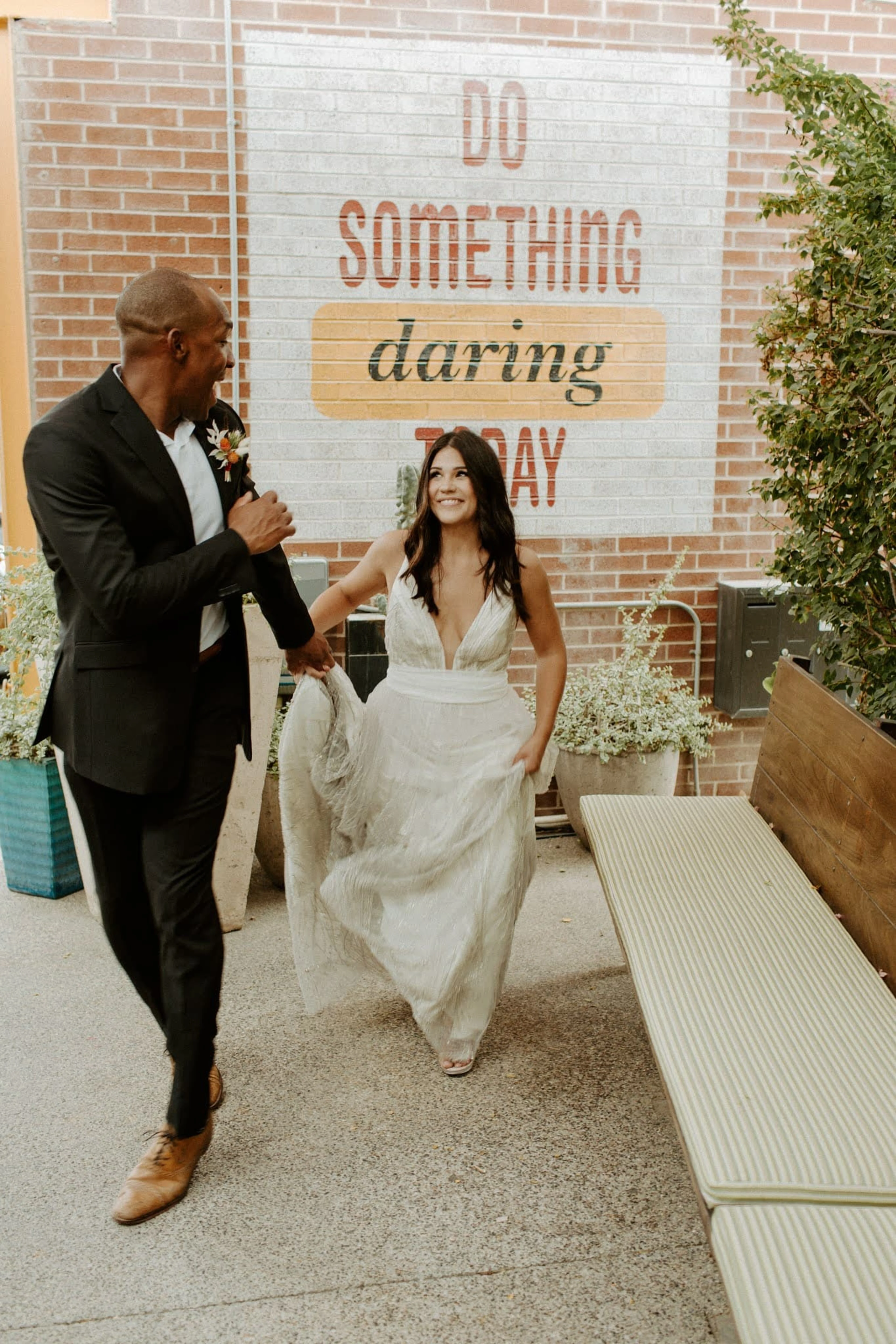 A bride and groom smile while walking and holding hands.
