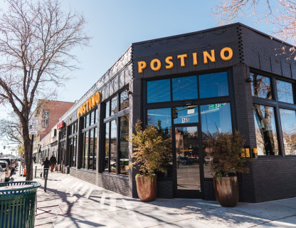 A dark colored building with a yellow Postino sign.